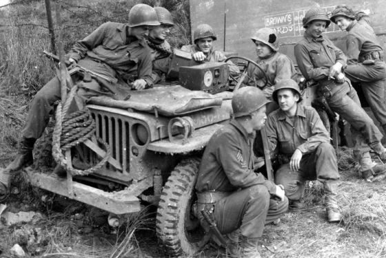 Soldiers by a Jeep, listen to a game on the radio